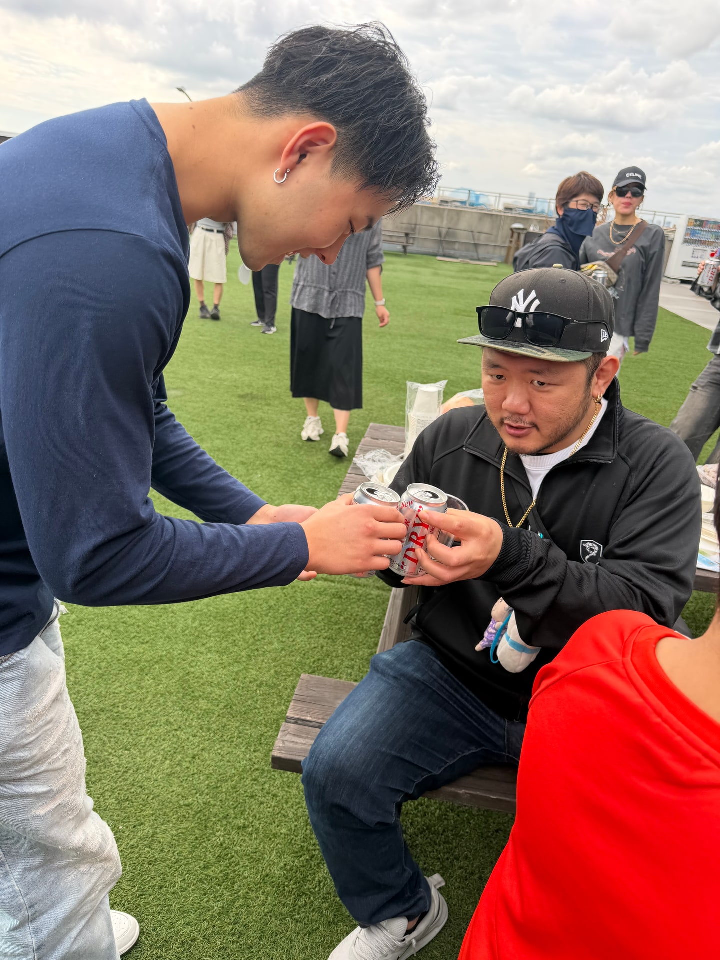 缶ビールを手渡しながら乾杯している様子