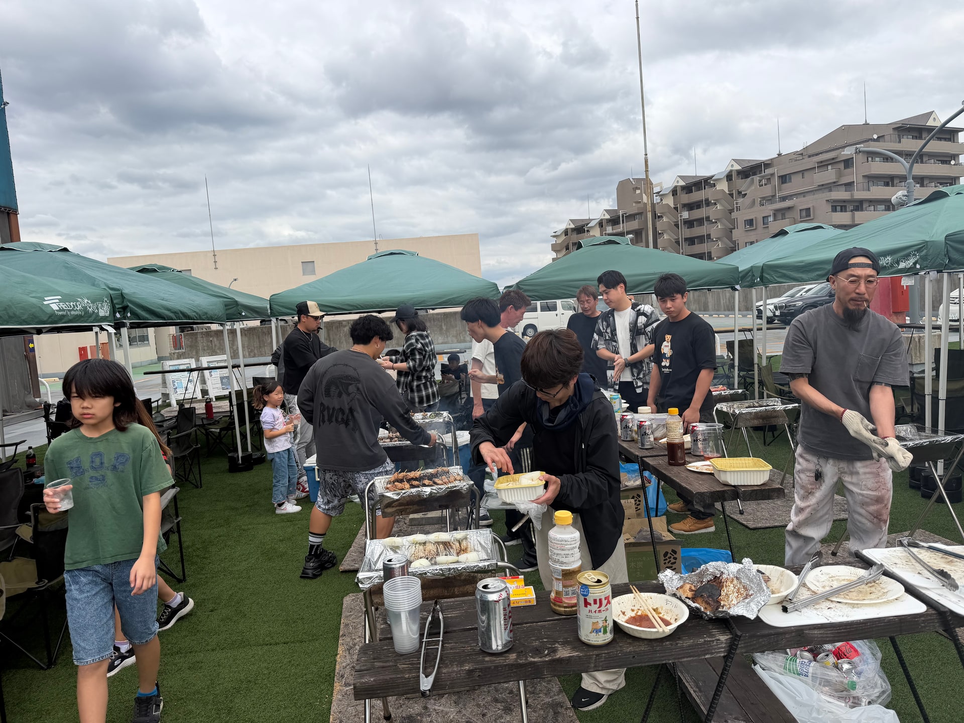 屋上でBBQグリルを囲み食材を焼いたり盛り付けたりしている様子