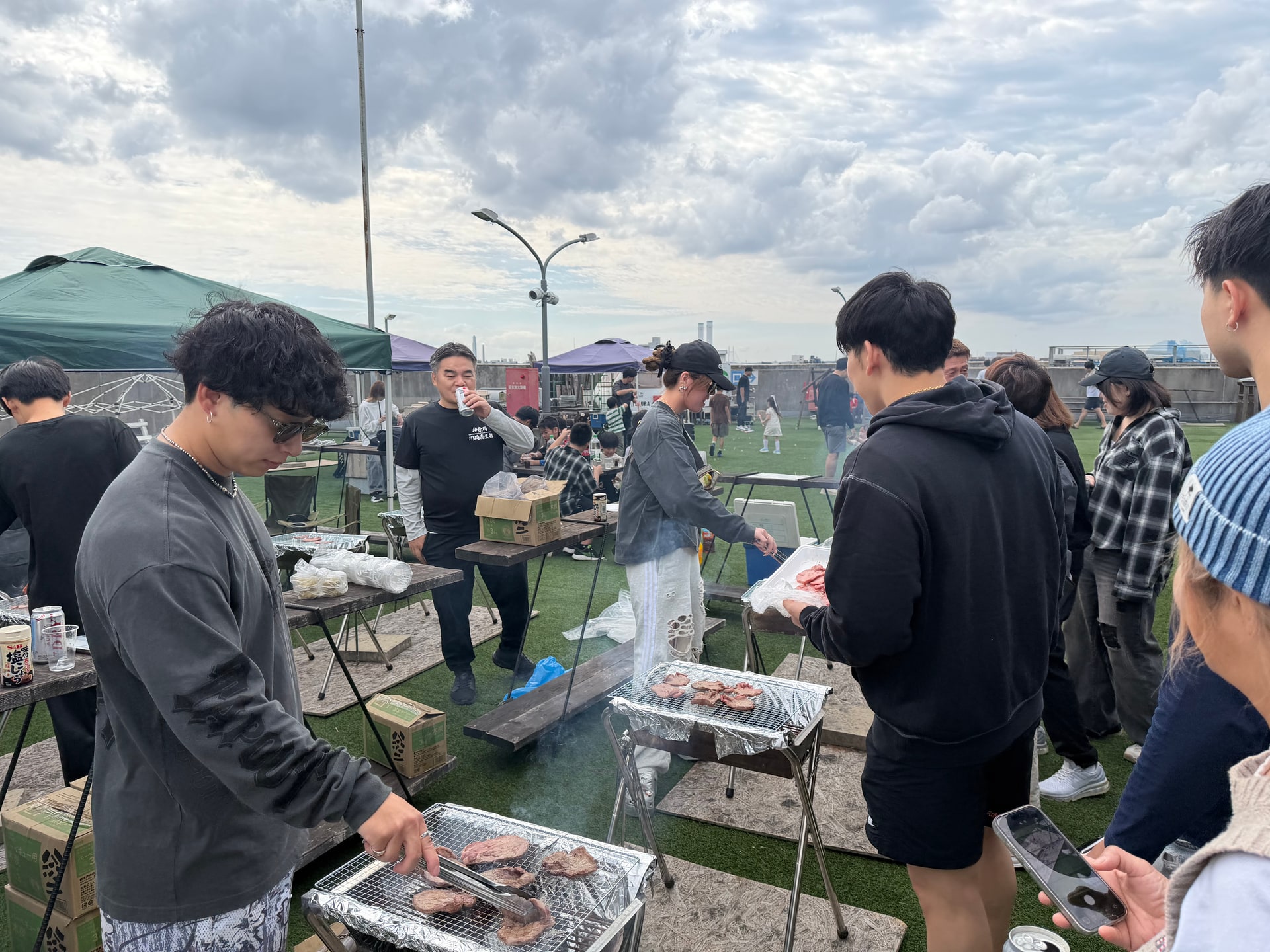 屋上でグリルを囲み肉を焼いている様子」class=